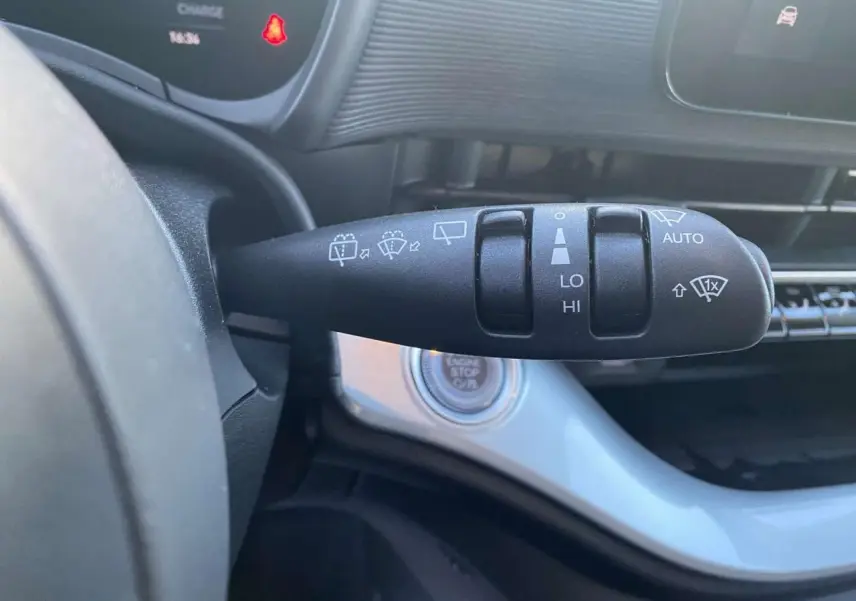 Gros plan sur la commande des essuie-glaces à gauche du volant dans l'habitacle noir de la Fiat 500 électrique 2022.