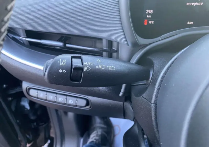 Gros plan sur la commande des phares et clignotants à gauche du volant dans l'habitacle noir d'une Fiat 500 électrique.