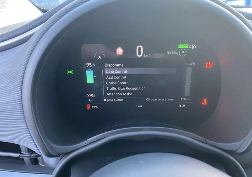Tableau de bord numérique de la Fiat 500 électrique noire, affichant les aides à la conduite et l'autonomie restante.