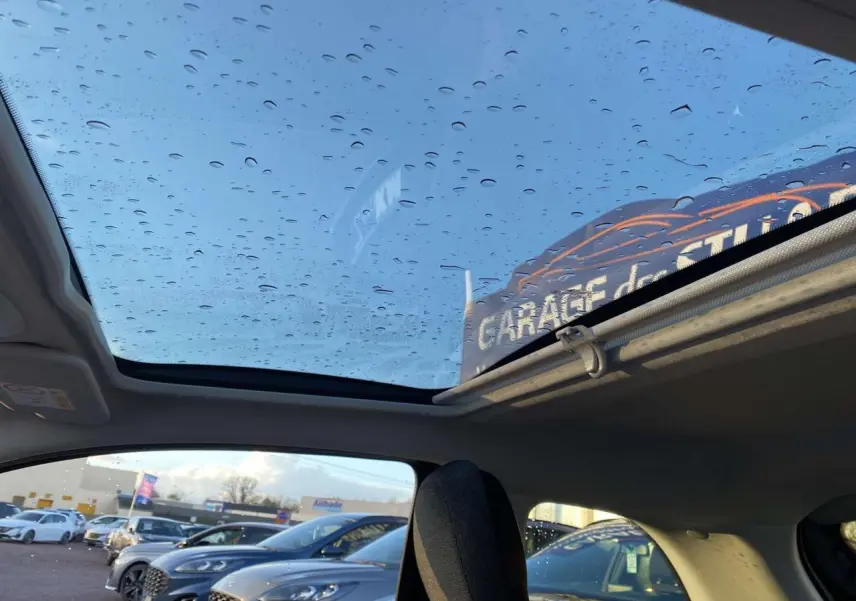 Toit vitré panoramique avec gouttes d'eau sur une Fiat 500 électrique noire, vue intérieure côté arrière droit.