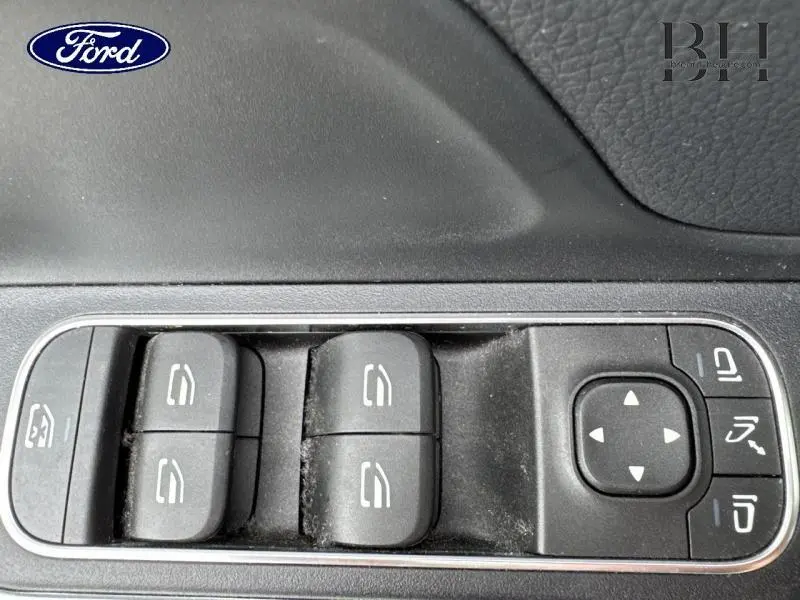 Gros plan sur les commandes de lève-vitres et rétroviseurs d'une Mercedes GLA 250 e bleu denim métallisé.