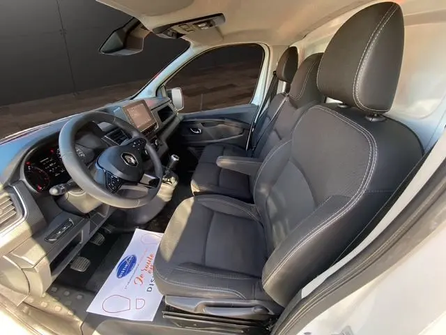 Vue intérieure côté conducteur du Renault Trafic Fourgon blanc 2023, montrant les sièges noirs et le tableau de bord moderne.