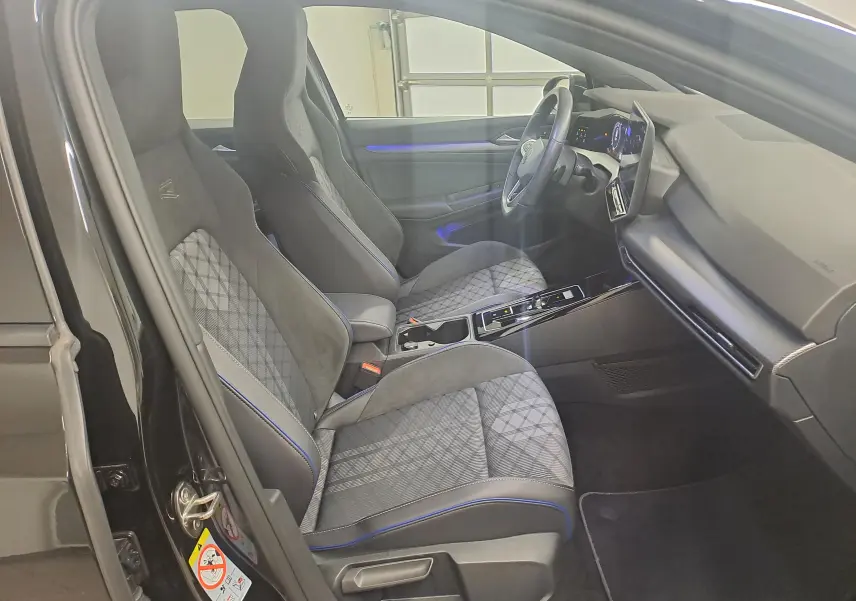 Vue intérieure côté conducteur de la Volkswagen Golf 2.0 TDI R Line 2024, sièges sport noirs avec surpiqûres bleues et tableau de bord moderne.