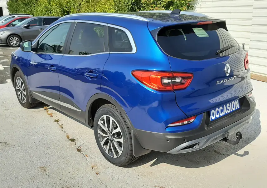 Renault Kadjar bleu Iron en 3/4 arrière droit, avec feux arrière LED et attelage visible sur parking extérieur.