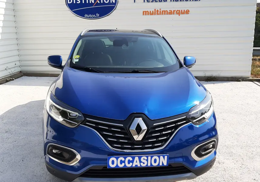 Vue avant d'un Renault Kadjar bleu iron 2020 avec plaque "OCCASION" devant un mur publicitaire Distinxion.