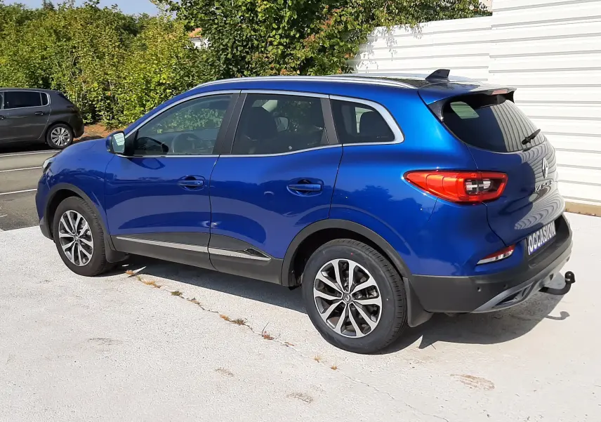Renault Kadjar bleu Iron vu en 3/4 arrière côté droit, avec jantes alliage et attelage visible.