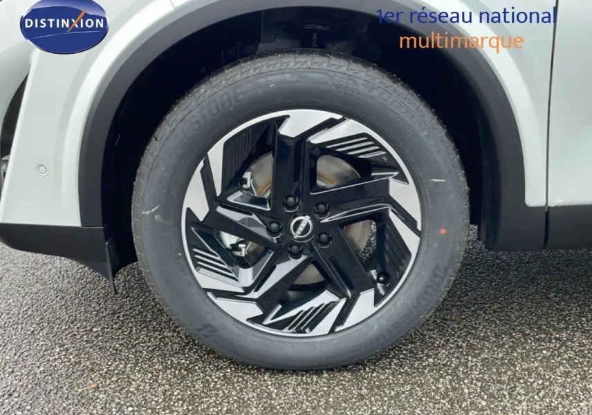 Gros plan sur la roue avant gauche du Nissan Qashqai blanc nacré, avec jante alliage noire et argentée au design moderne.