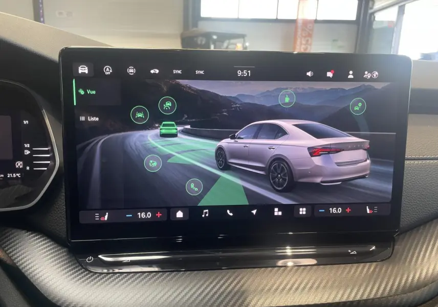 Écran tactile du tableau de bord montrant une Skoda Octavia blanche en vue 3/4 arrière sur route sinueuse.