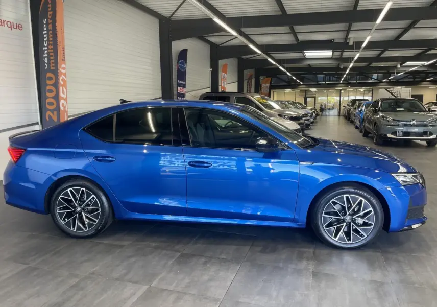 Vue latérale droite d'une Skoda Octavia 2025 bleu foncé avec jantes alliage noires et vitres teintées dans un showroom.