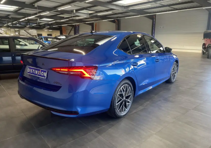 Vue 3/4 arrière droite d'une Skoda Octavia Sportline bleu foncé avec jantes alliage noires et feux arrière LED allumés.