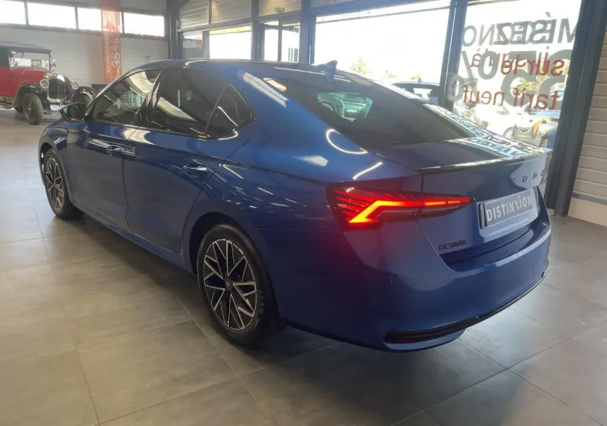 Vue 3/4 arrière droite d'une Skoda Octavia 2025 bleu foncé avec feux arrière LED allumés en intérieur showroom.