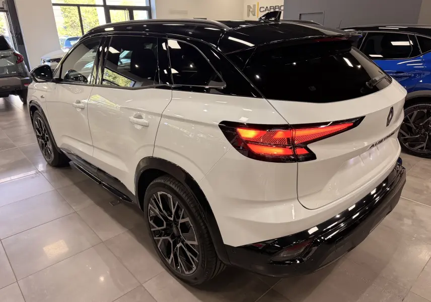 Vue 3/4 arrière droite du Renault Austral blanc nacré avec toit noir et feux arrière LED allumés en showroom.