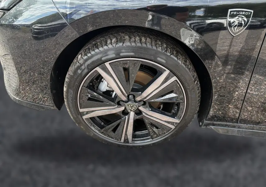 Gros plan sur la roue avant droite noire d'une Peugeot 308 1.2 hybrid 145 GT avec jante alu au design moderne et logo Peugeot visible.
