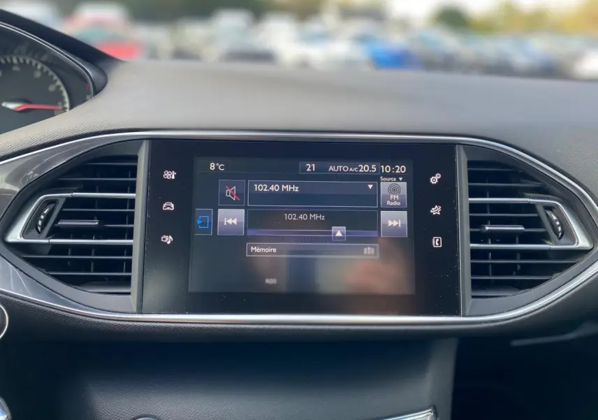 Écran tactile central de la Peugeot 308 2016 affichant la radio FM, entouré de grilles d'aération noires.