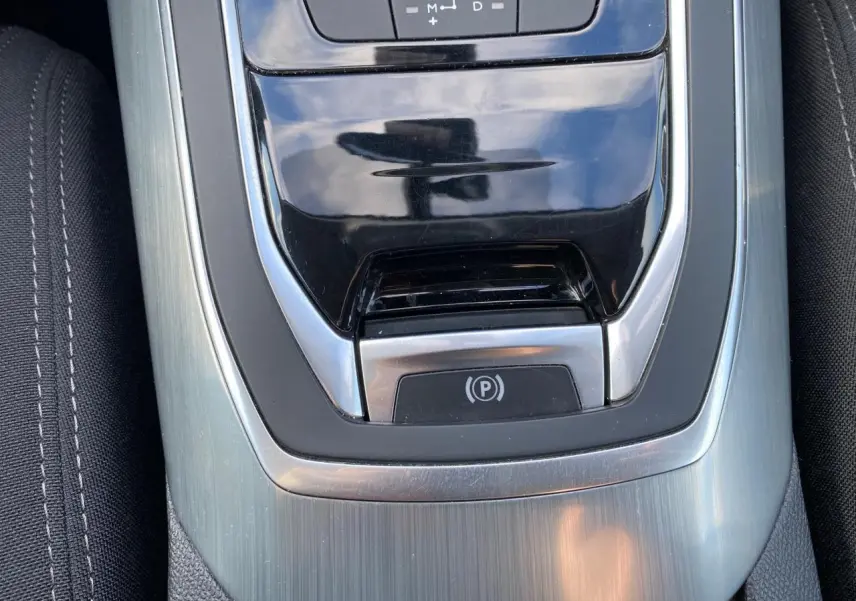 Gros plan sur la console centrale de la Peugeot 308 gris aluminium, mettant en valeur le frein de parking électrique et la finition métallique.