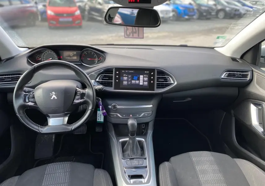 Vue intérieure avant de la Peugeot 308 2016, tableau de bord noir avec volant cuir et écran tactile central.