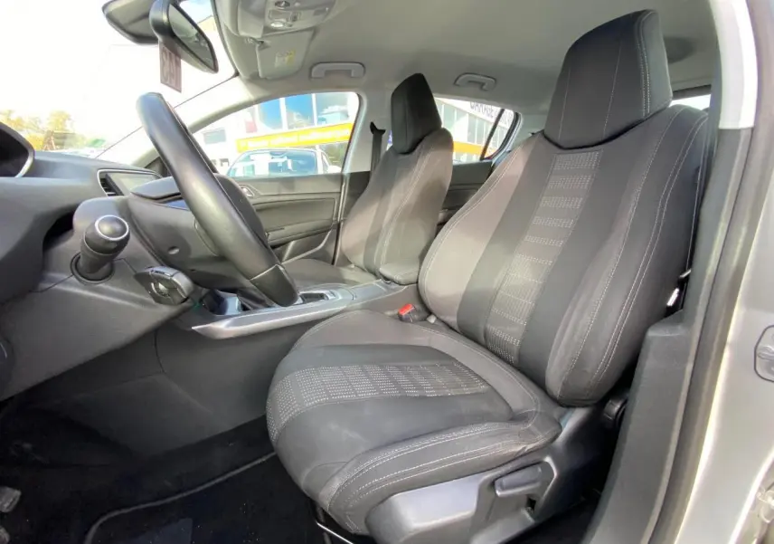 Vue intérieure côté conducteur de la Peugeot 308 gris aluminium, montrant les sièges avant en tissu et le volant cuir sport.