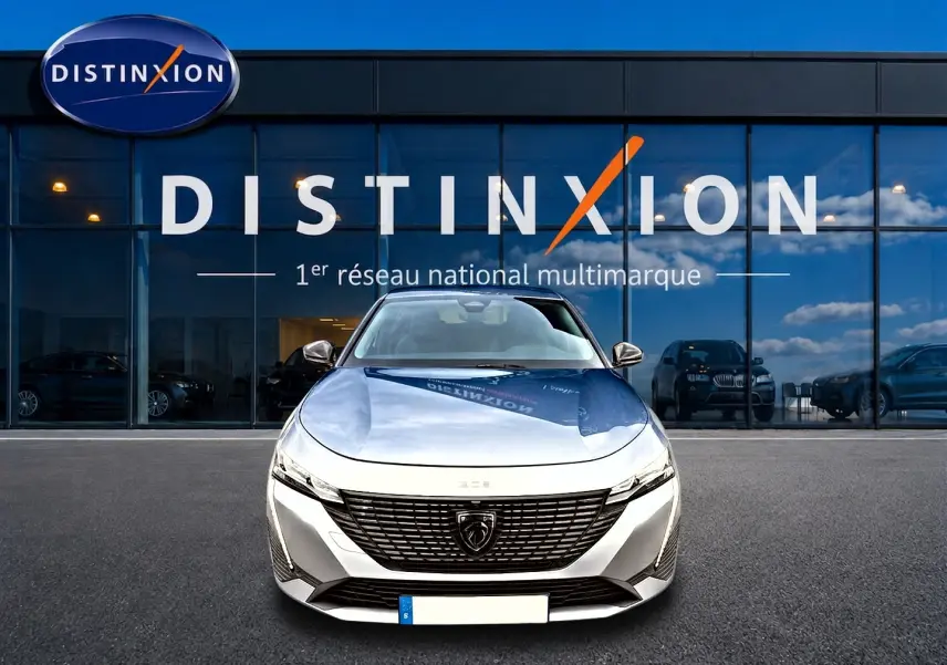 Vue avant d'une Peugeot 308 gris artense avec calandre noire et logo lion, devant une vitrine Distinxion.
