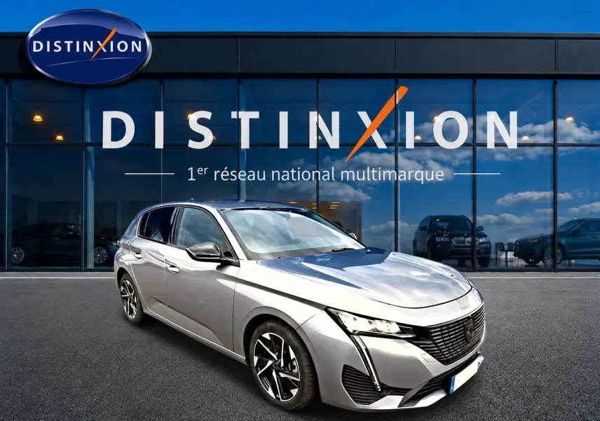 Peugeot 308 gris artense vue 3/4 avant droit, avec jantes alu et feux LED distinctifs, devant showroom Distinxion.