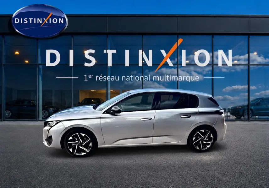 Profil droit d'une Peugeot 308 gris artense 2025 garée devant une vitrine Distinxion, avec jantes alu noires et chromées.