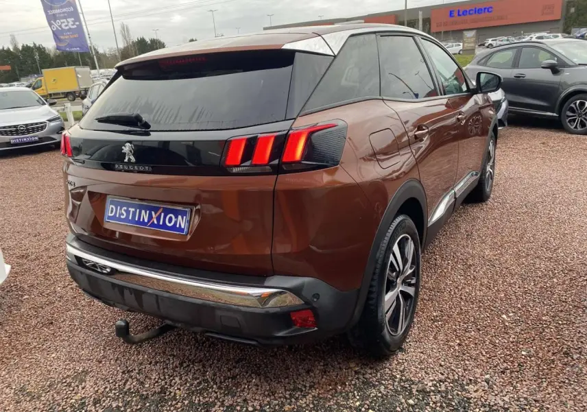 Peugeot 3008 marron foncé vue 3/4 arrière droit avec attelage et jantes alliage 18 pouces sur parking.