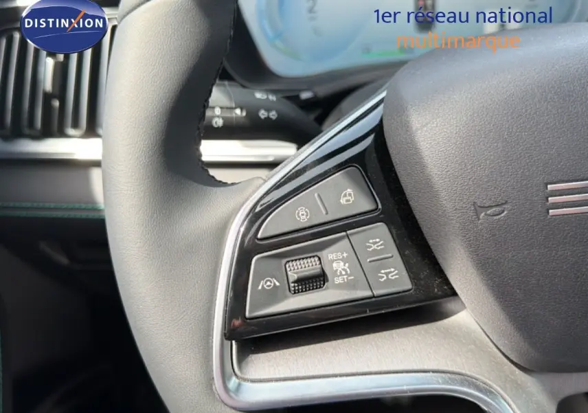 Gros plan sur les commandes à gauche du volant noir du BYD SEAL U hybride rechargeable blanc métal, tableau de bord en arrière-plan.