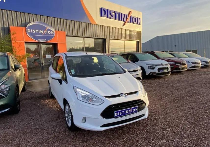Vue 3/4 avant d'une Ford B-MAX blanche garée devant un concessionnaire Distinxion par temps clair.