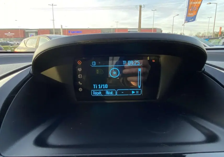 Écran central du tableau de bord de la Ford B-MAX blanc 2014 affichant les commandes audio avec vue extérieure floue.