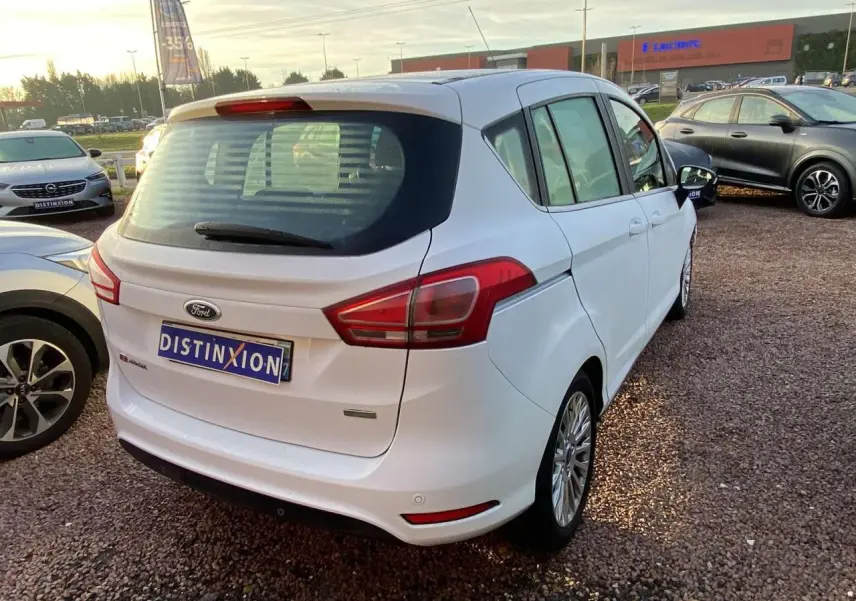 Ford B-MAX blanc vu en 3/4 arrière droit sur un parking, avec jantes alliage et feux arrière distinctifs.