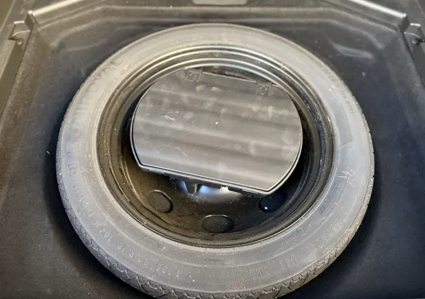 Gros plan sur la roue de secours dans le coffre d'un Opel Grandland X gris quartz, montrant le pneu et son rangement.