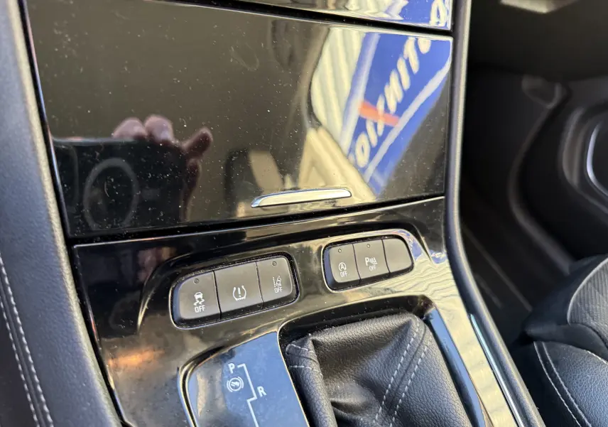 Gros plan sur la console centrale noire brillante de l’Opel Grandland X gris quartz, montrant les boutons de contrôle et le levier de boîte automatique.