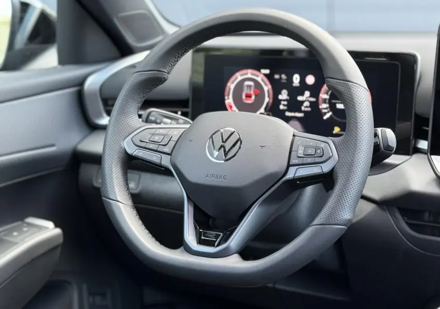 Volant sport multifonction en cuir noir avec logo Volkswagen, tableau de bord numérique en arrière-plan, intérieur T-Roc 2026.