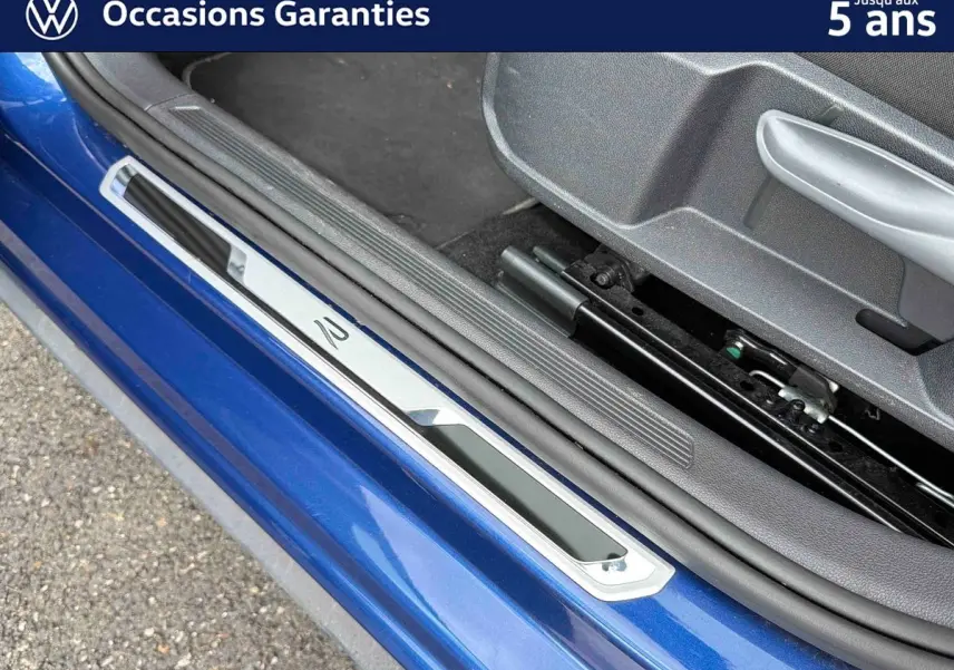 Détail de la porte côté conducteur d’une Volkswagen Polo bleue métallisée avec seuil de porte en métal et intérieur gris.