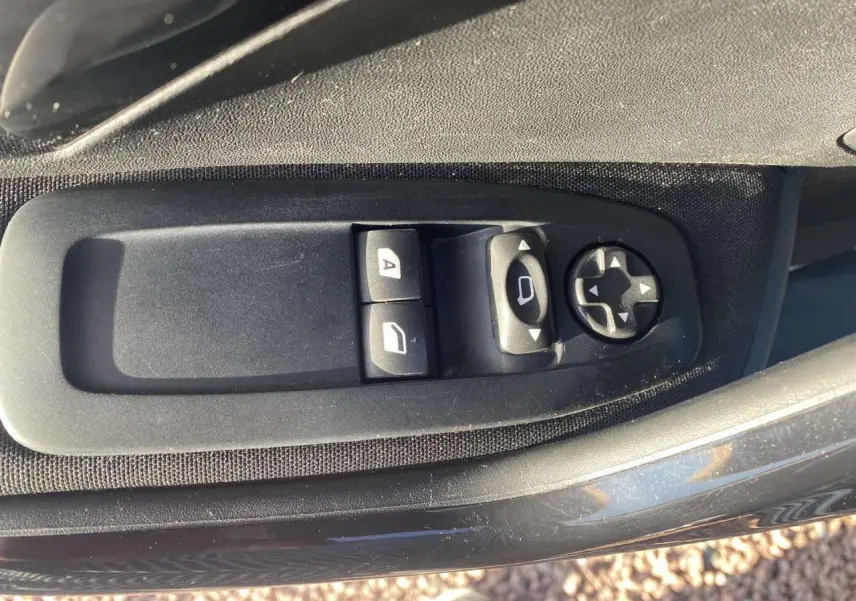 Gros plan sur les commandes électriques des vitres et des rétroviseurs côté conducteur d'une Peugeot 208 noire.