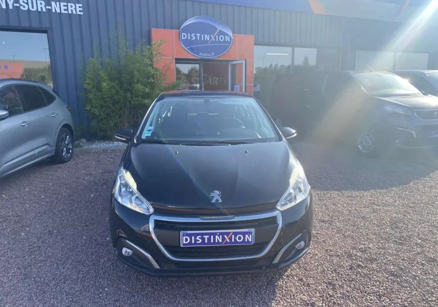 Vue avant d'une Peugeot 208 noire 2016 avec calandre chromée et phares allumés sur parking extérieur.