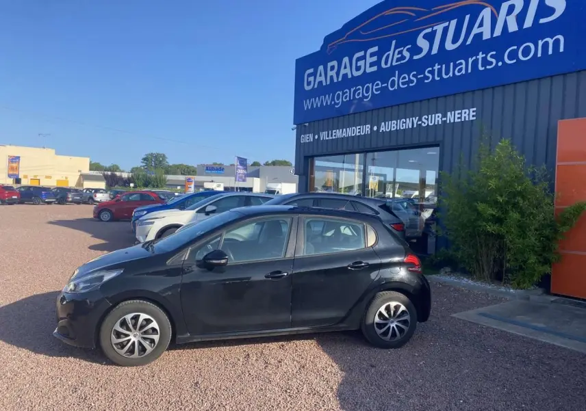 Peugeot 208 noire vue de profil côté gauche, garée devant un garage avec jantes acier 15 pouces et peinture métallisée.