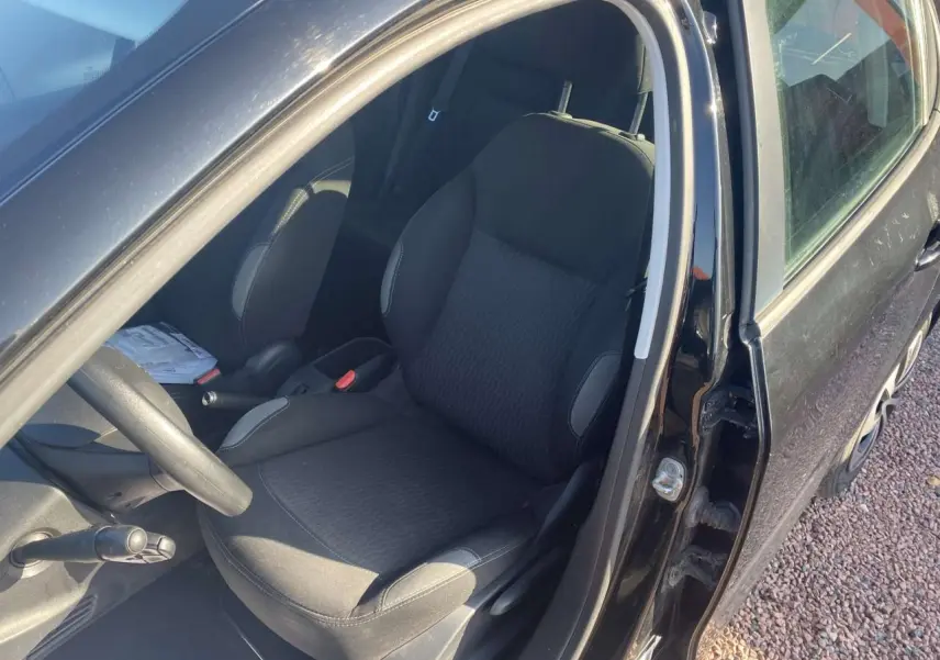 Vue intérieure côté conducteur de la Peugeot 208 noire de 2016, siège avant et volant multifonction visibles.