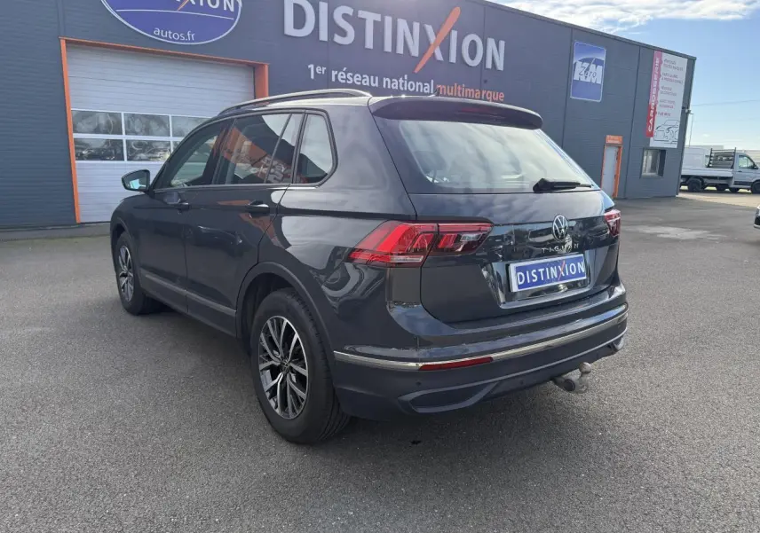 Vue 3/4 arrière droite d'un Volkswagen Tiguan gris Urano avec crochet d'attelage et jantes alliage foncé brillant.