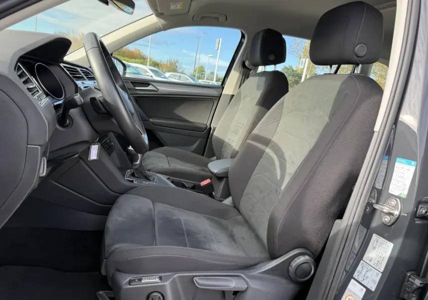 Vue intérieure côté conducteur du Volkswagen Tiguan 2023 gris Urano, sièges ergoActive en tissu et alcantara noirs.
