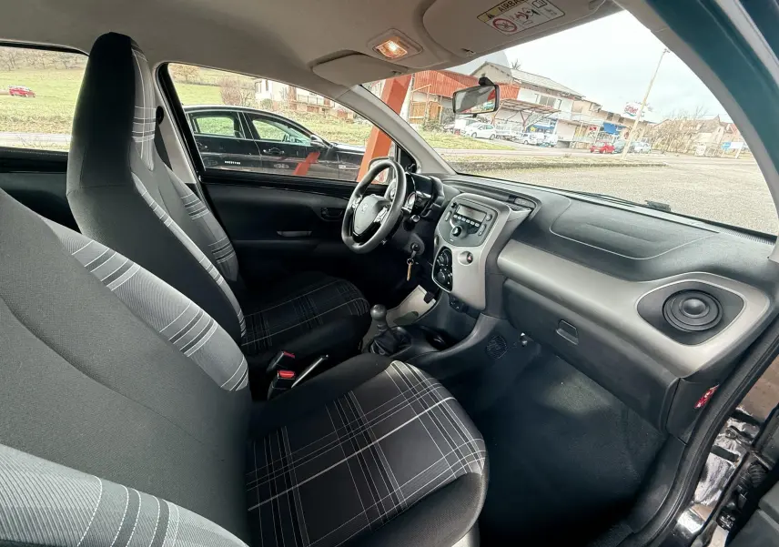 Intérieur avant du Peugeot 108 noir 2018, vue côté conducteur montrant sièges en tissu gris à motifs et tableau de bord simple.