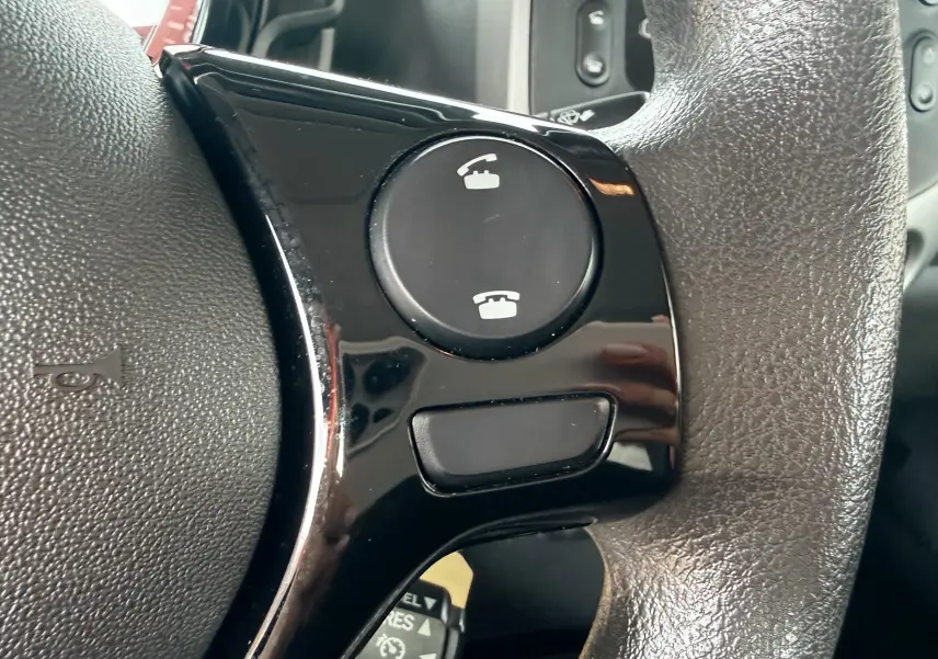 Gros plan sur les commandes téléphoniques noires intégrées au volant en cuir d'une Peugeot 108 noire de 2018.