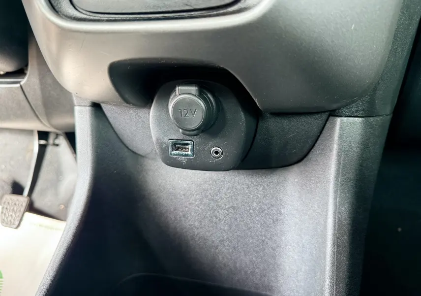 Prise 12V, port USB et entrée auxiliaire sous le tableau de bord d'une Peugeot 108 noire, vue intérieure côté conducteur.