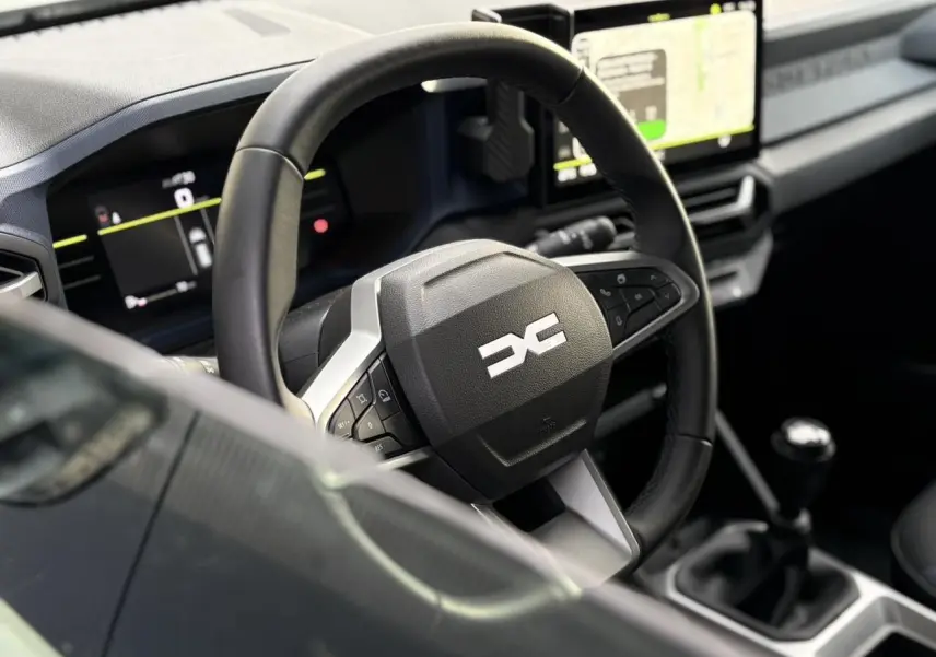 Vue rapprochée du volant et tableau de bord digital du Dacia Duster 2024, intérieur noir avec écran tactile.