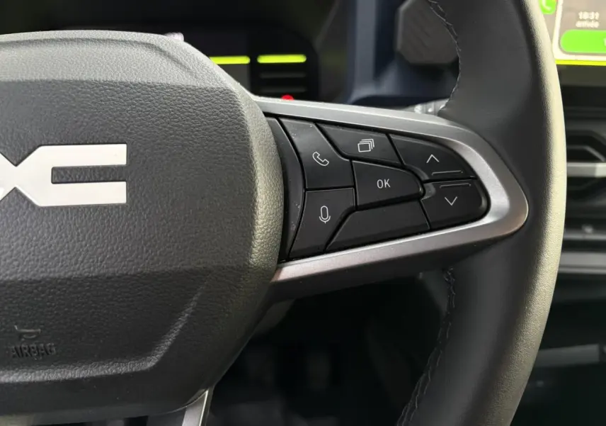 Gros plan sur les commandes au volant droit en cuir noir du Dacia Duster beige Sandstone 2024, avec écran tactile visible.