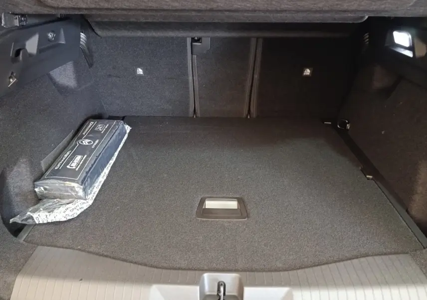 Coffre spacieux de Citroën C5 Hybride 2026, vue intérieure, tapis gris foncé avec kit de sécurité sur le côté.