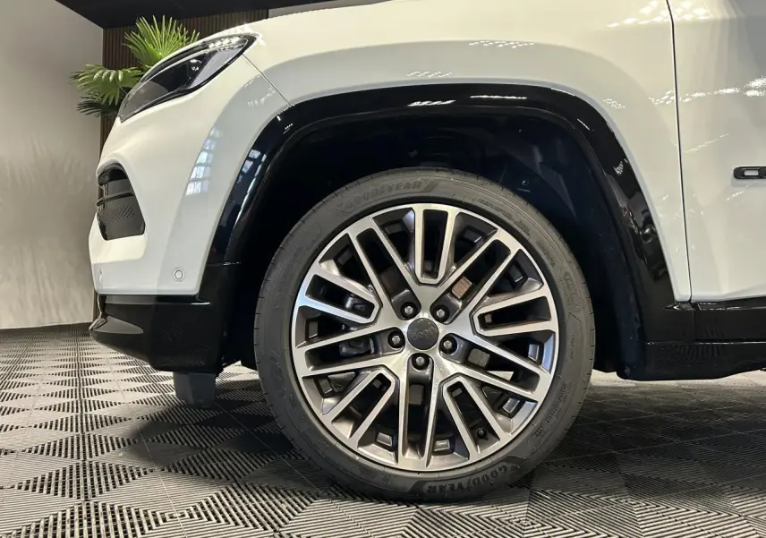 Gros plan sur la roue avant droite avec jante alliage 19'' du Jeep Compass blanc, soulignant l'aile et le pare-chocs noir.