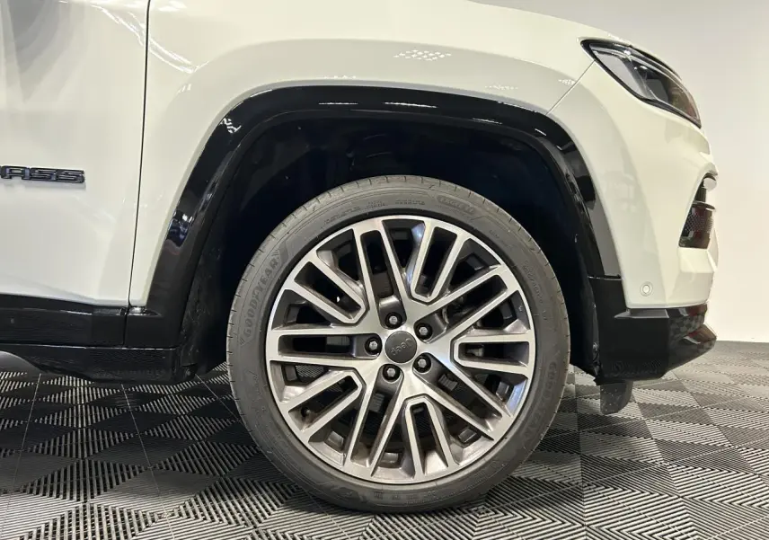 Gros plan sur la roue avant droite en jante alliage 19'' du Jeep Compass blanc avec entourage noir brillant.