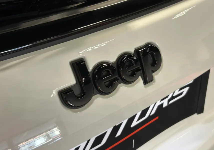 Gros plan sur le logo Jeep noir brillant sur la carrosserie blanche Alpine White du Compass 2024.