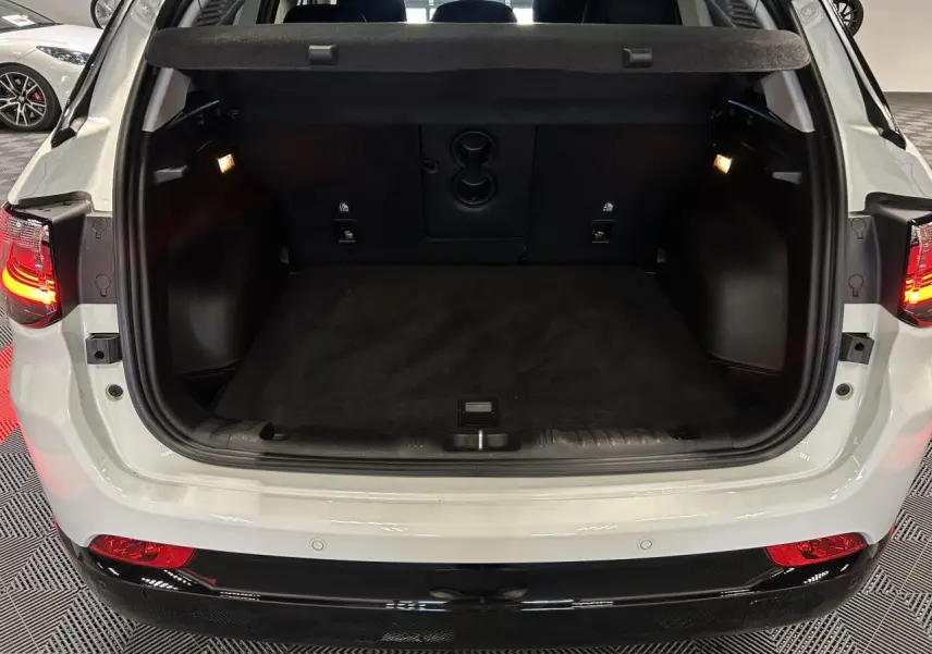 Coffre ouvert vu de l'arrière d'un Jeep Compass blanc avec intérieur noir et feux arrière allumés.