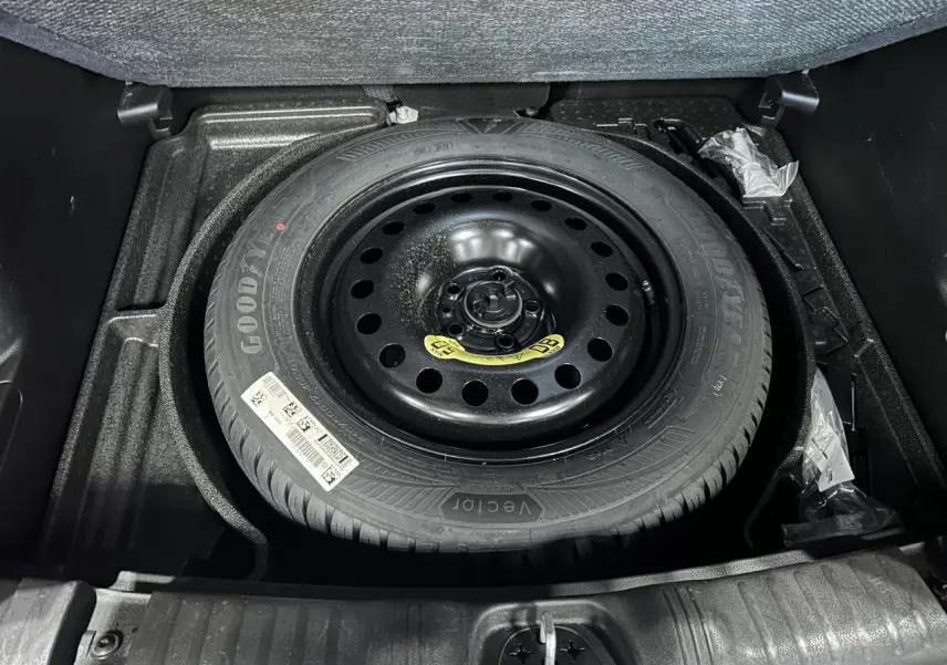 Roue de secours temporaire noire dans le coffre du Jeep Compass 2024 blanc, vue en plongée sur le pneu Goodyear.